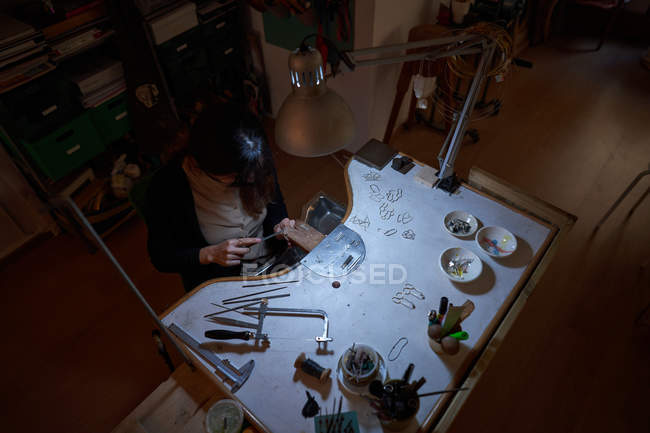 Beautiful Artisan Jeweler Woman Working In A Jewelry Shop With Tools And A Light Bulb Person Manufacturing Stock Photo