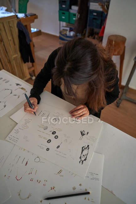 From above woman sitting at a table with a pencil drawing jewels on paper — Stock Photo