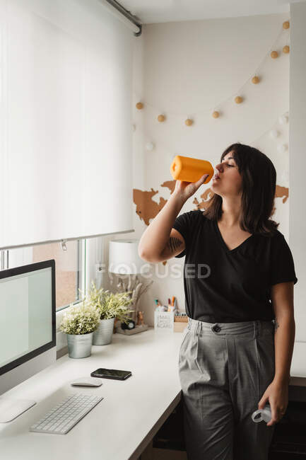 Sedienta empleada adulta bebiendo agua en el lugar de trabajo - foto de stock