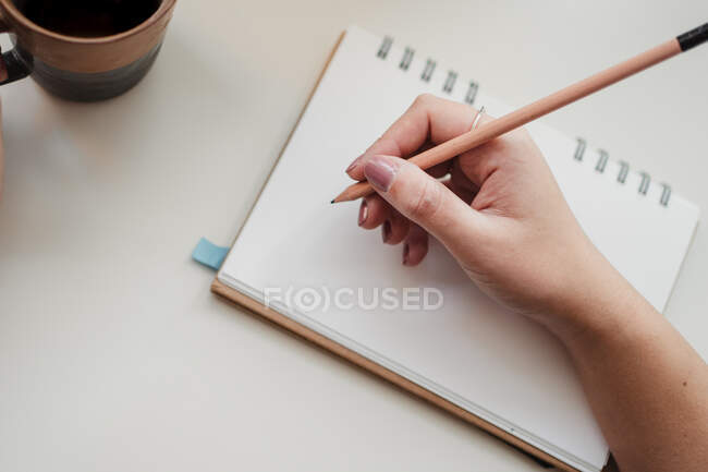 Freelancer femenina sin rostro haciendo notas en la mesa en el lugar de trabajo - foto de stock