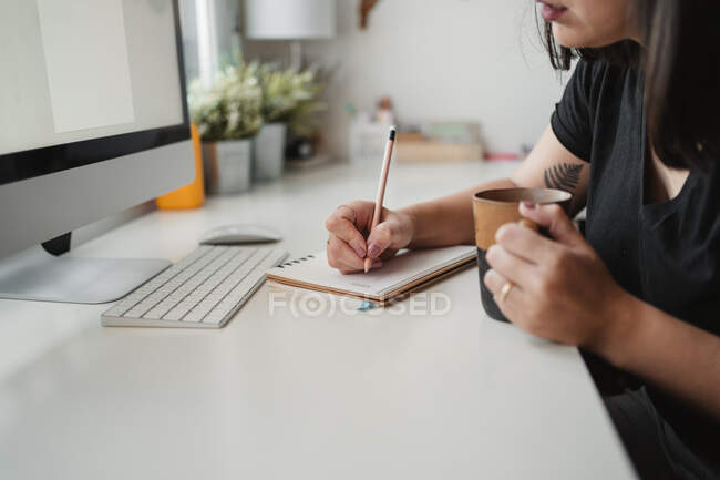 Faceless female freelancer making notes at table at workplace — Stock Photo
