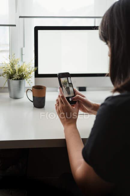 Mujer anónima tomando fotos en el teléfono inteligente en el lugar de trabajo - foto de stock
