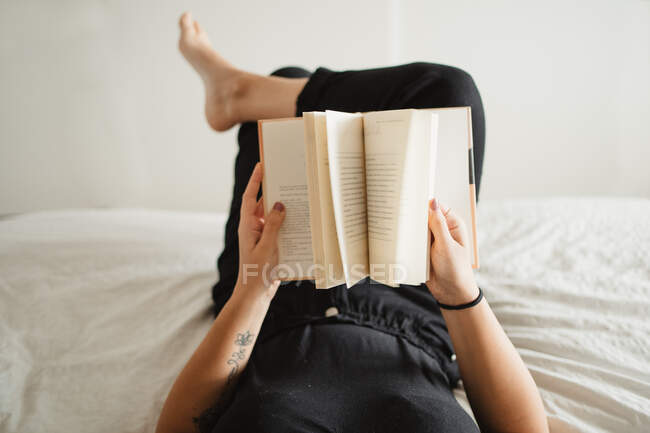 Femme méconnaissable lecture livre sur le lit à la maison — Photo de stock