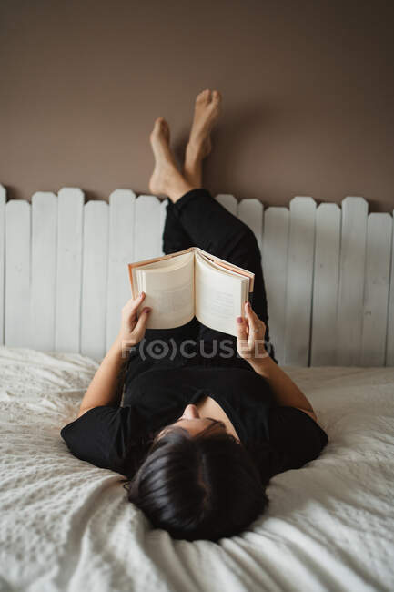 Unerkennbare Frau liest Buch zu Hause im Bett — Stockfoto