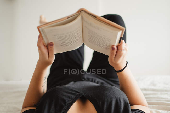 Mulher irreconhecível lendo livro na cama em casa — Fotografia de Stock