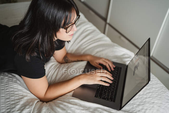 Focalizzato giovane studentessa utilizzando il computer portatile sul letto a casa — Foto stock