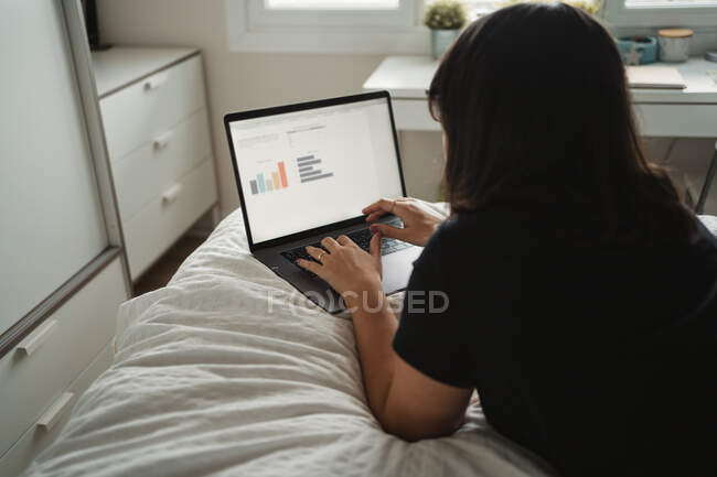 Focalizzato giovane studentessa utilizzando il computer portatile sul letto a casa — Foto stock