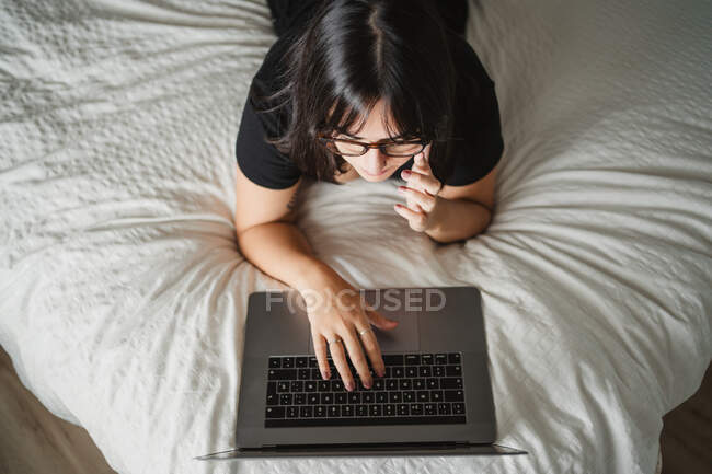 Орієнтована молода студентка використовує ноутбук на ліжку вдома — стокове фото