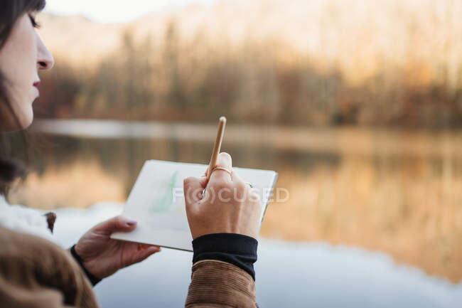 Mujer de pie junto al lago y dibujando en cuaderno - foto de stock