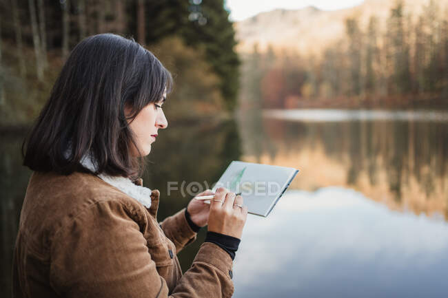 Woman standing at lakeside and drawing in notebook — Stock Photo