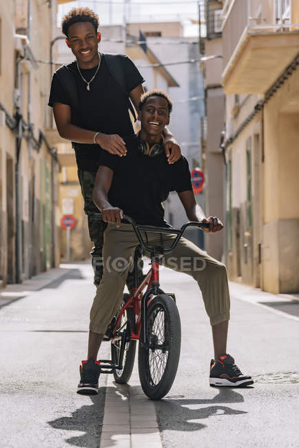 Happy youthful African American male teenagers having fun while riding on BMX bike together in street — Stock Photo