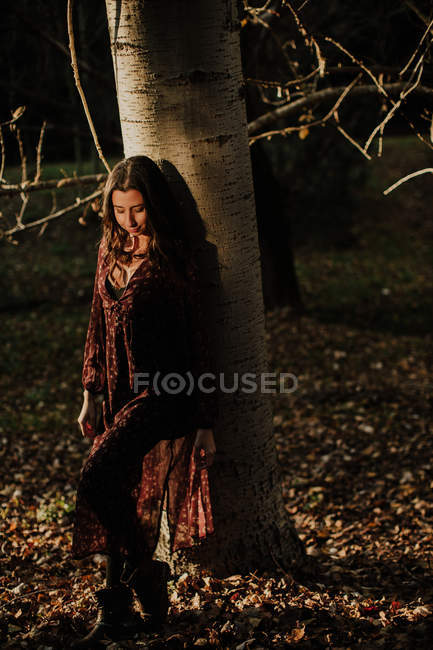 Femme agréable en tenue décontractée touchant feuille jaune automne et souriant dans les bois — Photo de stock