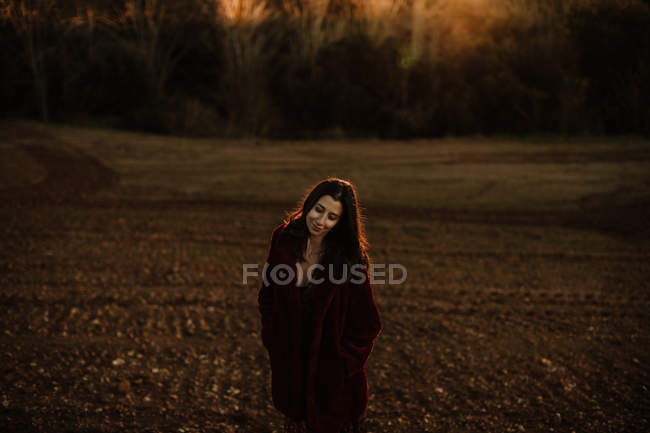 Joyful woman in warm coat smiling and looking at camera while walking along autumn forest — Stock Photo