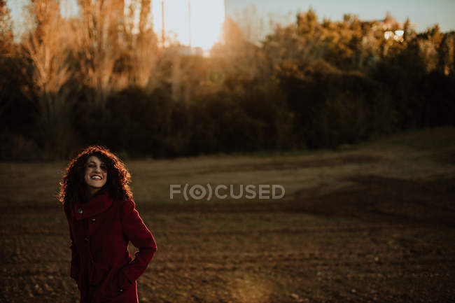 Joyful redhead woman in warm coat smiling and looking at camera while walking along autumn forest — Stock Photo