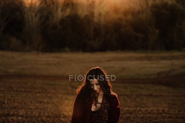 Радостная женщина в теплом пальто улыбается и смотрит в камеру во время прогулки по осеннему лесу — стоковое фото