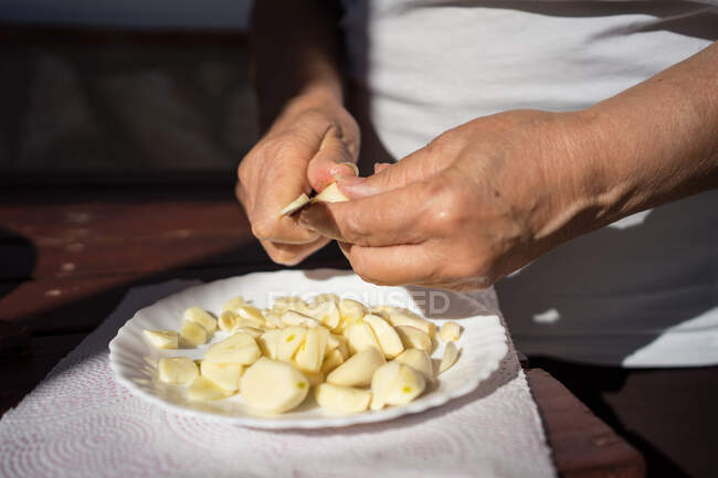 Person schneidet geschälten Knoblauch in Teller auf Tisch — Stockfoto