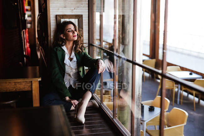 From above of pensive trendy woman sitting with crossed legs and looking through window of modern cafe — Stock Photo