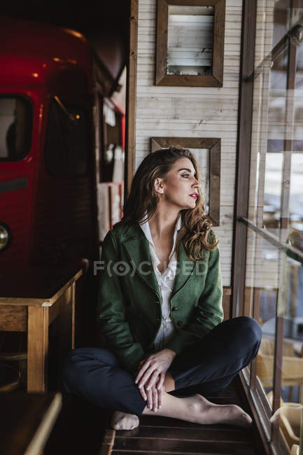Von oben von nachdenklicher trendiger Frau, die mit gekreuzten Beinen sitzt und durch das Fenster eines modernen Cafés blickt — Stockfoto