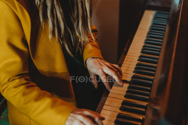 Cropped image of hipster with dreadlocks wearing yellow coat playing piano while sitting in retro styled room — Stock Photo