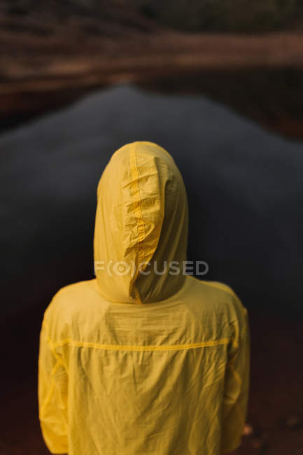 Traveler in yellow raincoat standing on shore of lake — Stock Photo