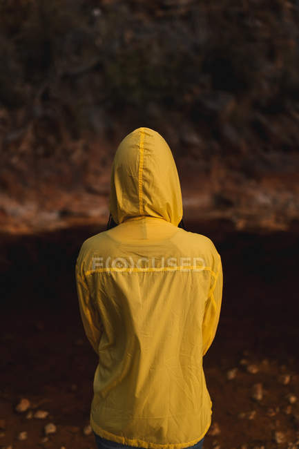 Mujer joven en impermeable amarillo paseando en la naturaleza - foto de stock