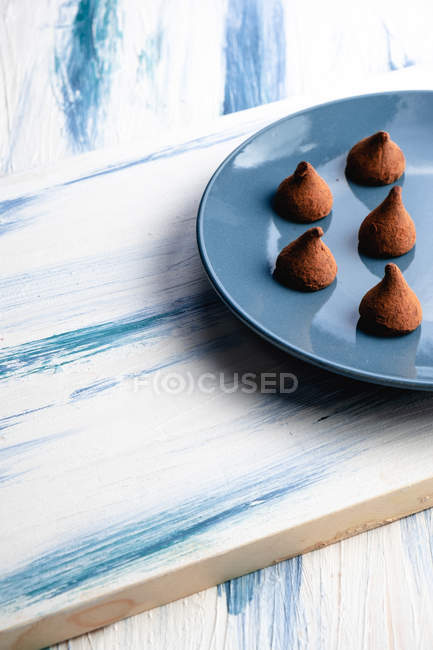 D'en haut plaque demi-bleue avec des bonbons au chocolat en forme de cône maison sur table rustique en bois — Photo de stock