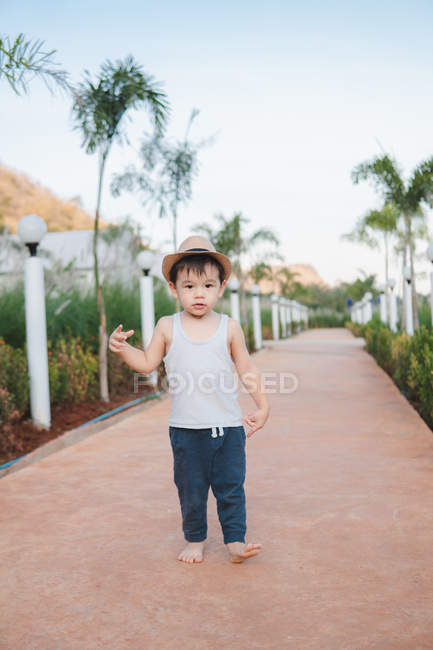 Sério asiático menino em casual desgaste e chapéu gestos andando descalço na rua olhando para a câmera — Fotografia de Stock