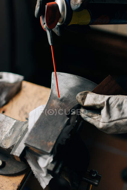 Faceless man with can of spray working on axe — Stock Photo