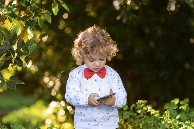 Цікавий маленький хлопчик переглядає смартфон у парку — стокове фото
