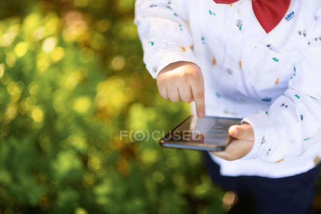 Curieux petit garçon naviguant smartphone dans le parc — Photo de stock