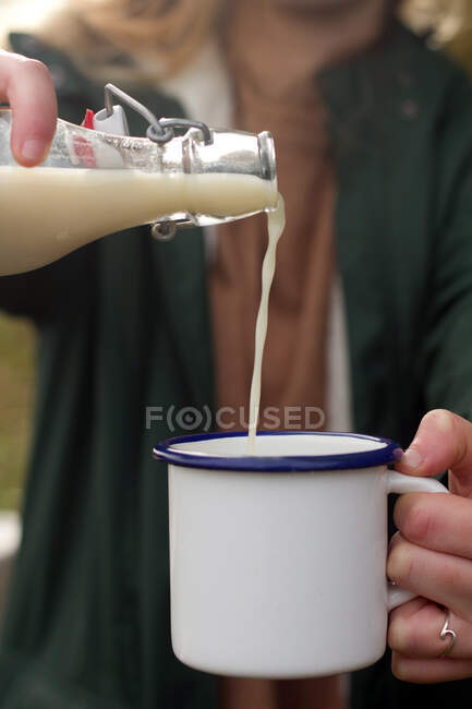 Mulher anônima enchendo caneca de leite durante piquenique — Fotografia de Stock
