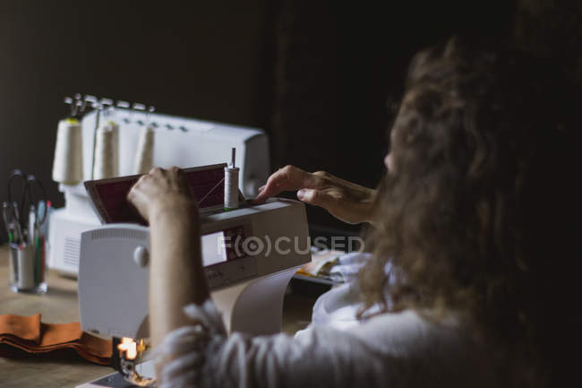 Visão traseira da mulher usando máquina de costura fazendo roupas sentadas à mesa em casa — Fotografia de Stock