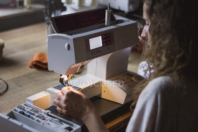 Vista trasera de la mujer con máquina de coser haciendo ropa sentada a la mesa en casa - foto de stock