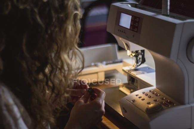 Back view of woman using sewing machine making clothes sitting at table in house — Stock Photo