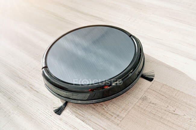 From above of round robotic vacuum cleaner sliding on light laminate floor — Stock Photo