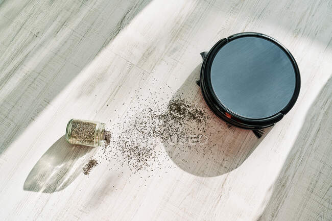 From above of round robotic vacuum cleaner sliding on light laminate floor and removing  dirt spilled out of glass pot — Stock Photo