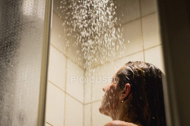 Вид сбоку обнаженной женщины с закрытыми глазами, принимающей длинный горячий душ и моющей волосы в ванной комнате — стоковое фото