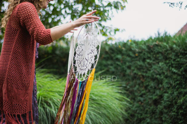 Mulher anônima em desgaste casual mostrando sonhadores artesanais com fios longos olhando para amuleto passar tempo no ar fresco — Fotografia de Stock