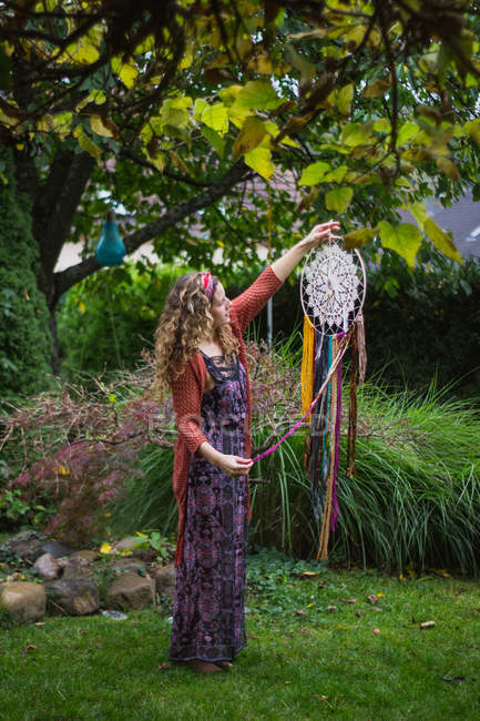 Mulher em desgaste casual mostrando handmade sonhadores com fios longos olhando para amuleto passar tempo no ar fresco — Fotografia de Stock