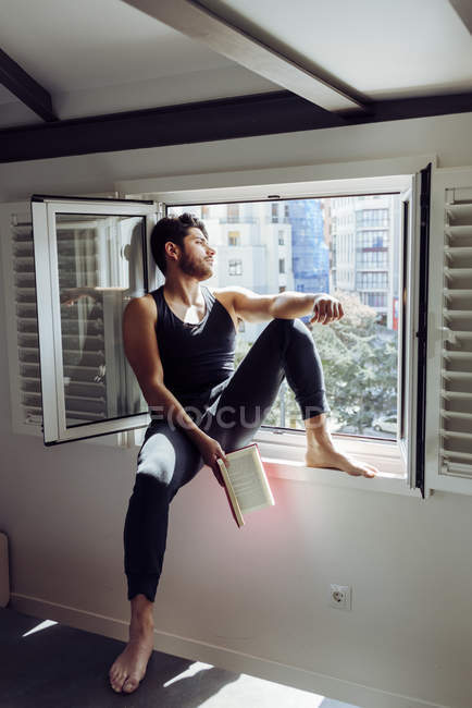 Young male sitting on window and reading book — Stock Photo