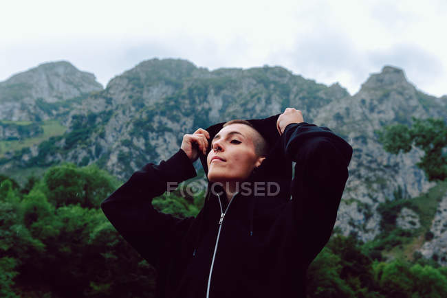 Woman with short hairstyle and piercing in casual clothing looking up to sky with pond among green plants on blurred background — Stock Photo
