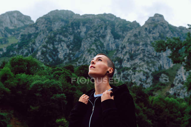 Жінка з короткою зачіскою і пірсингом в повсякденному одязі, дивлячись в небо з ставком серед зелених рослин на розмитому фоні — стокове фото