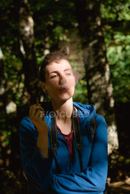 Female tourist resting and smoking marijuana joint while hiking in forest in summer — Stock Photo