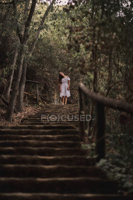 Знизу таємничої спокійної жінки в білій сукні, що стоїть на сходах у спокійному автономному парку — стокове фото