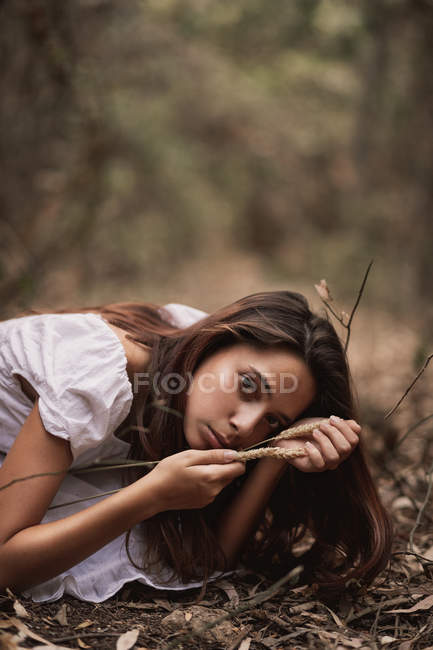 Чувственная таинственная женщина в белом платье сидит на коленях, прячась в осенней листве, глядя в камеру. — стоковое фото