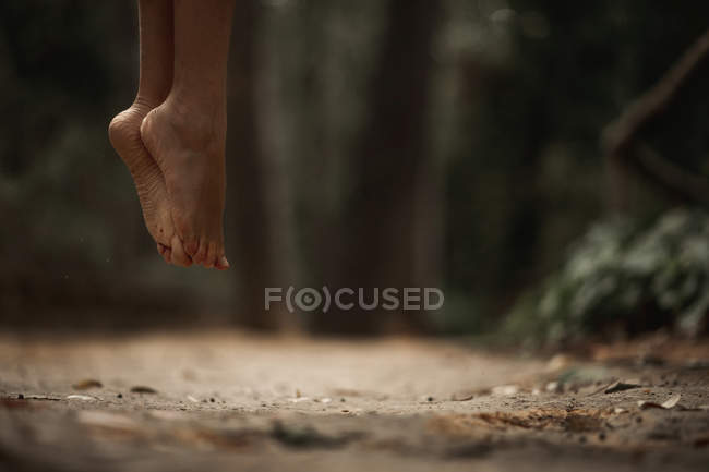 Imagem cortada de mulher pulando acima do solo na floresta outonal no fundo borrado — Fotografia de Stock
