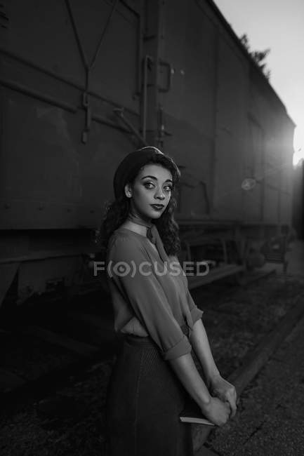 Жінка повністю носить одяг у старовинному стилі, що стоїть біля поїзда автомобіля і тримає відкриту книгу в руках — стокове фото
