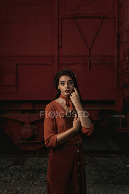Жінка повністю в теракотовому одязі в старовинному стилі стоїть біля поїзда з теракотовим автомобілем і тримає відкриту книгу в руках — стокове фото
