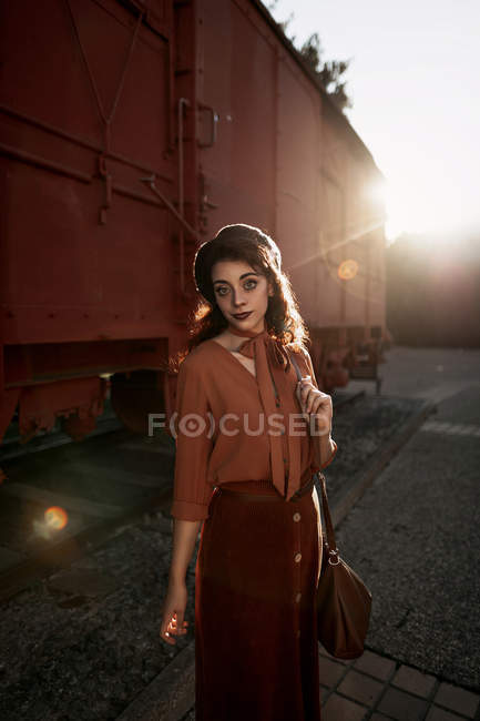 Mulher vestindo roupas de terracota em estilo vintage em pé perto de trem de carro de terracota e segurando livro aberto nas mãos — Fotografia de Stock