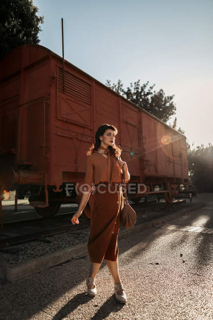 Femme portant des vêtements en terre cuite dans un style vintage debout près du train de voiture en terre cuite et tenant livre ouvert dans les mains — Photo de stock